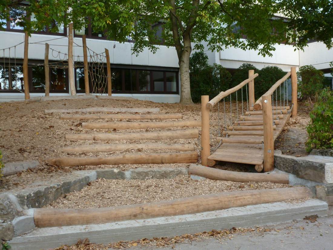 Holzstufen und eine kleine Hängebrücke aus Baumstämmen im Schulgarten