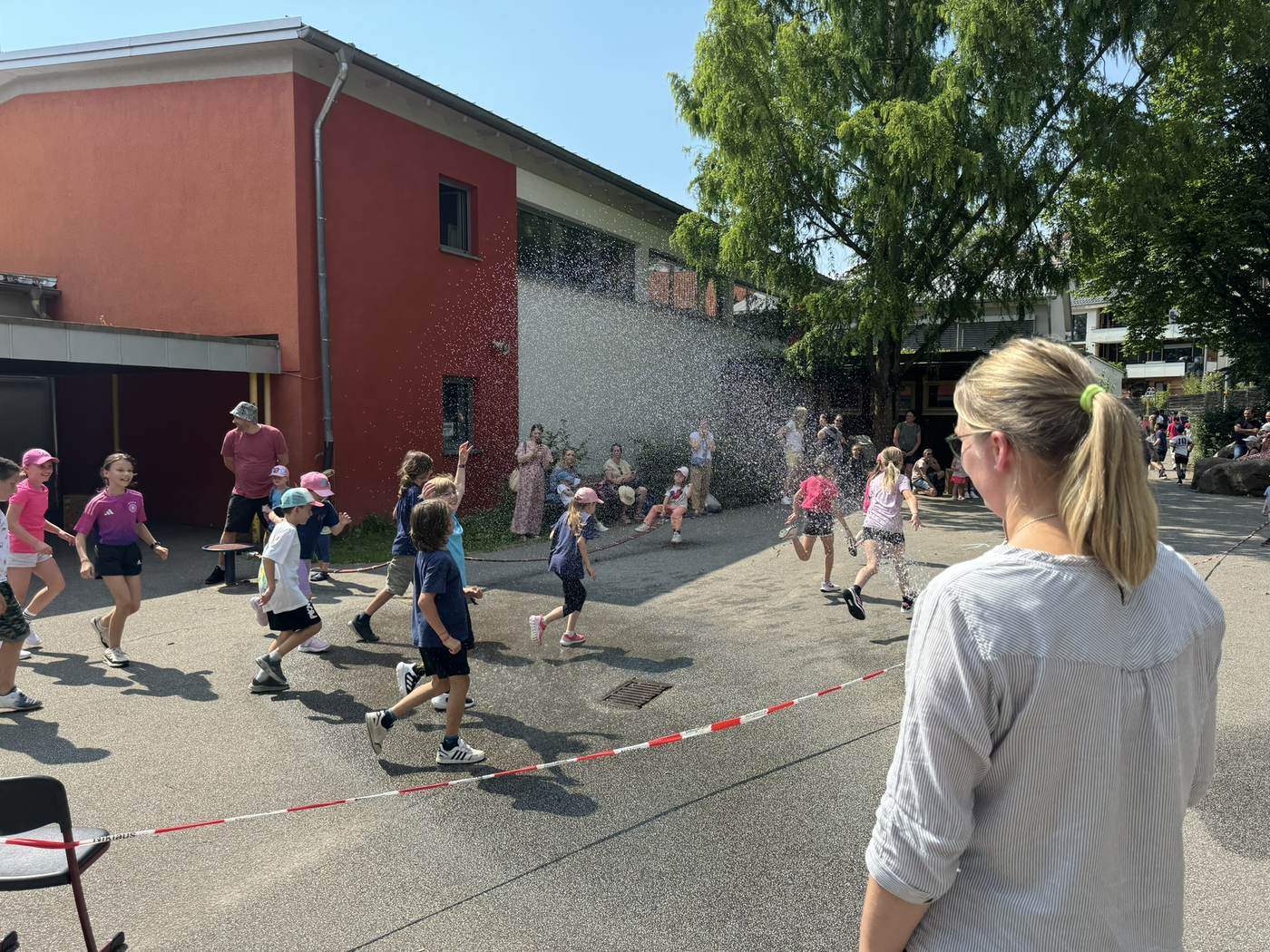 Kinder laufen beim Sponsorenlauf durch einen Wasserschauer auf dem Schulgelände